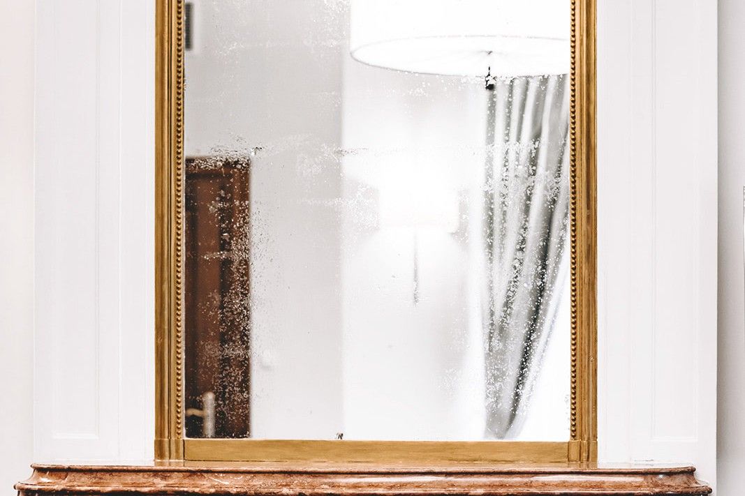 Ozdobne postarzane lustro w złotej ramie na marmurowym kominku w Pałacu Goetz
