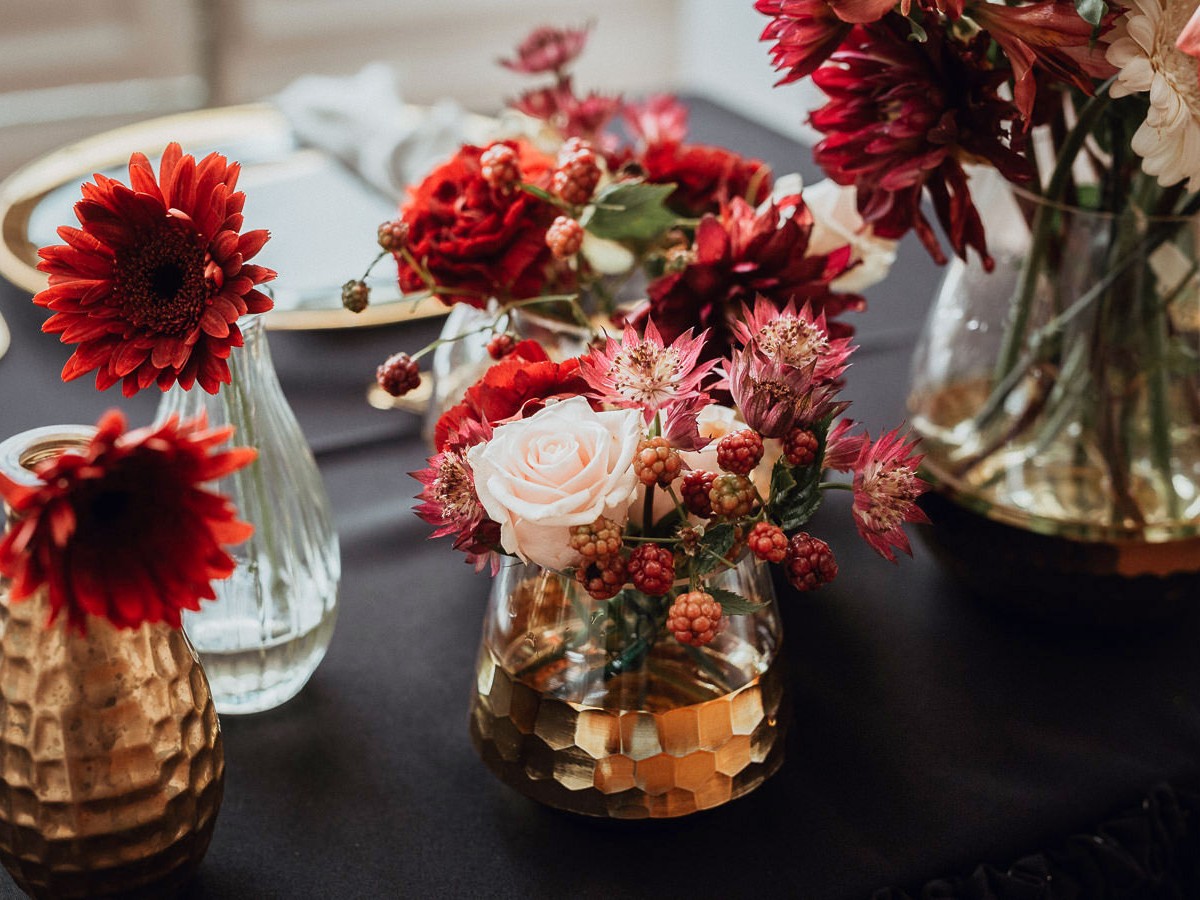 Czerwone kwiaty i złote dodatki w szklanych wazonach na stole podczas przyjęcia weselnego w Pałacu Goetz